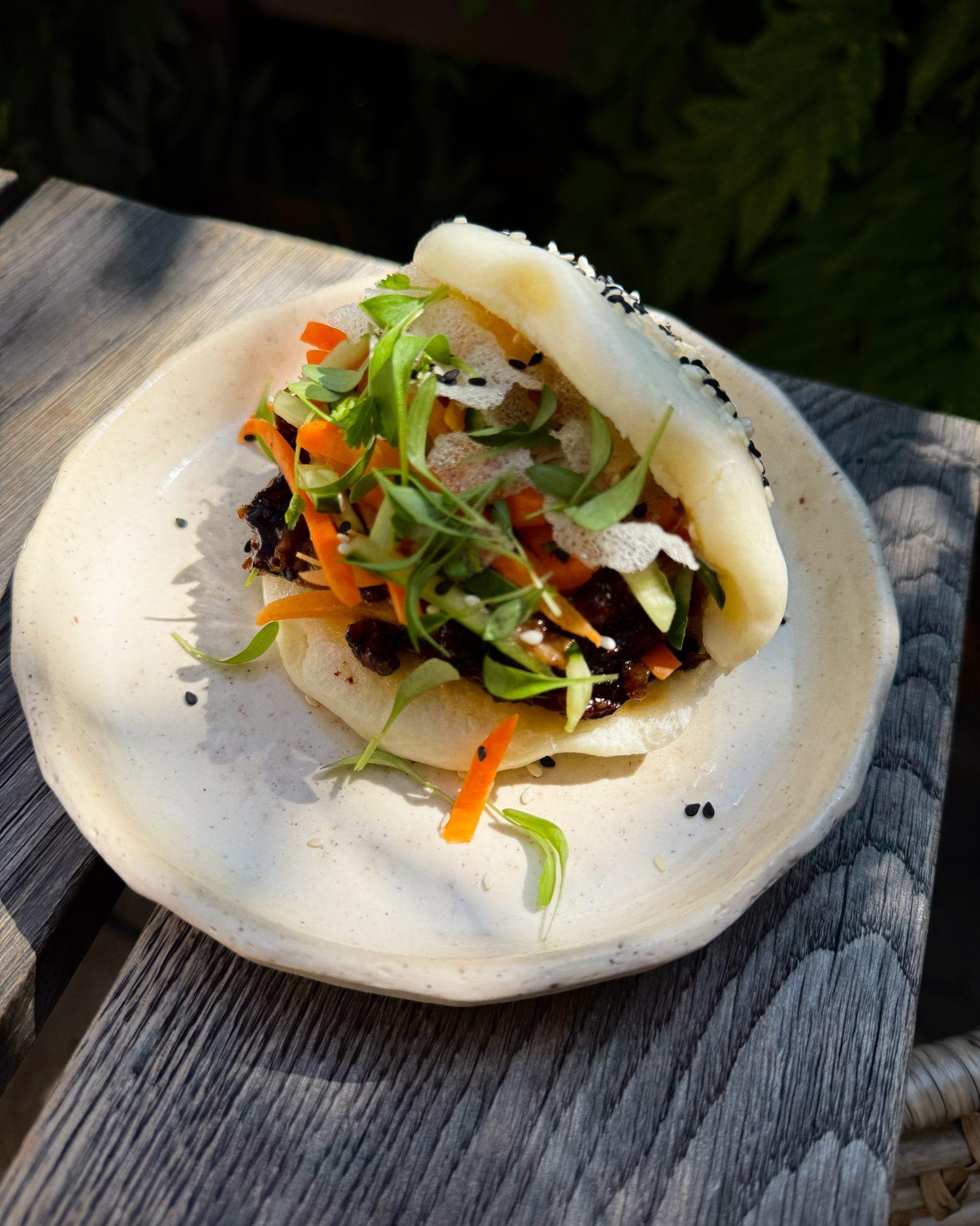 Bao bun s masem a zeleninou na keramickém talíři na zvětralém dřevě
