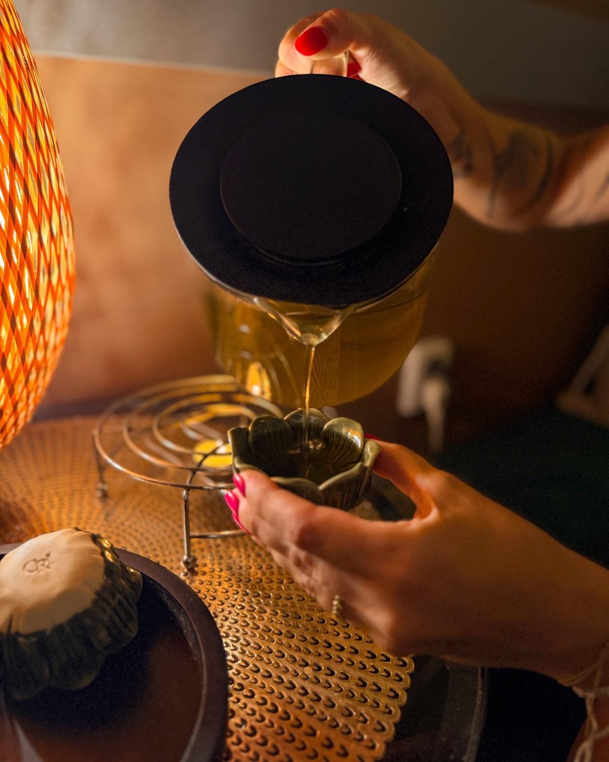 Nalévání čaje do misky ve tvaru lotosu ve světle proutěné lampy
